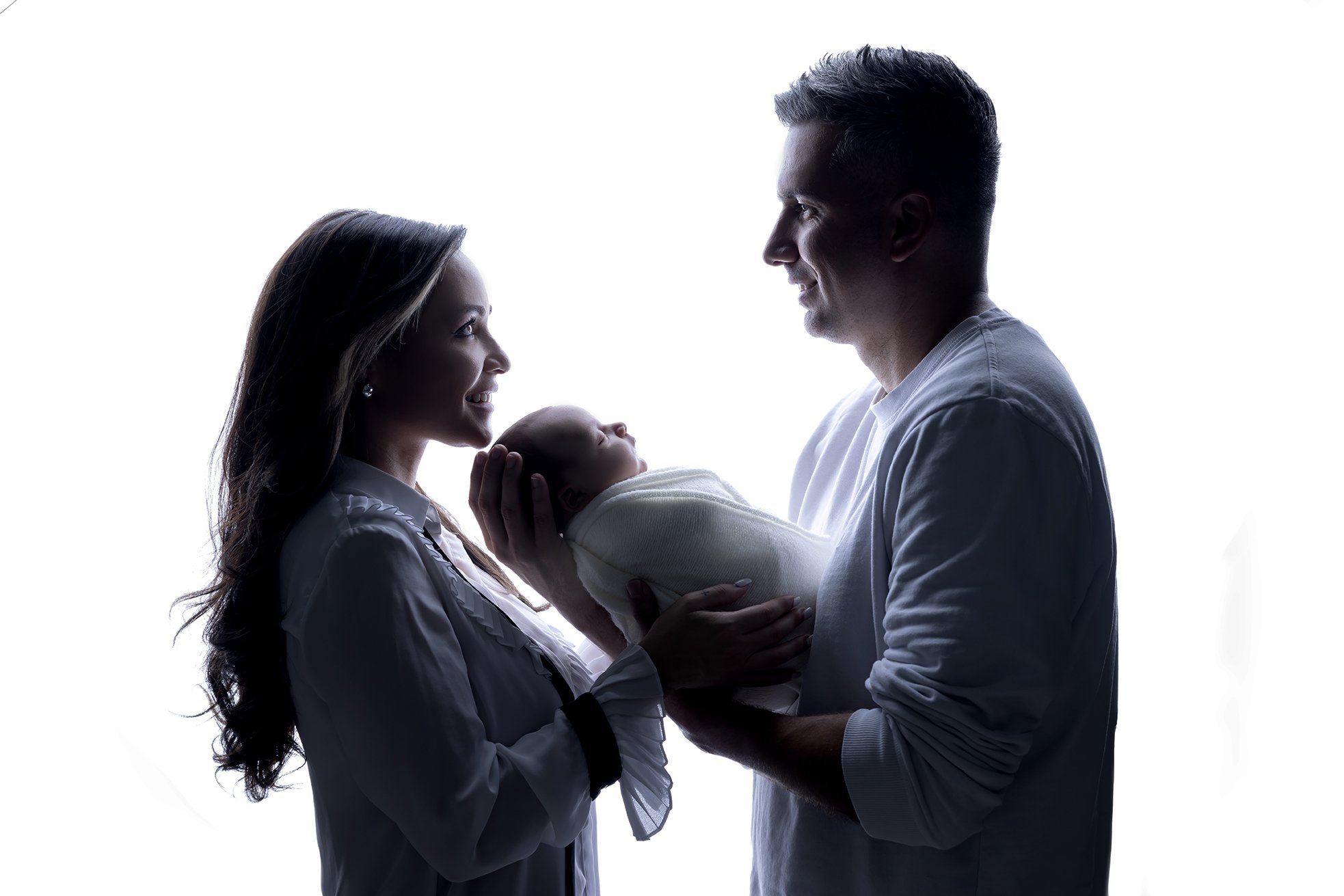 Silhouette of a family with a mother, father, and newborn baby, with the parents gazing at each other and holding the baby, against a white background.