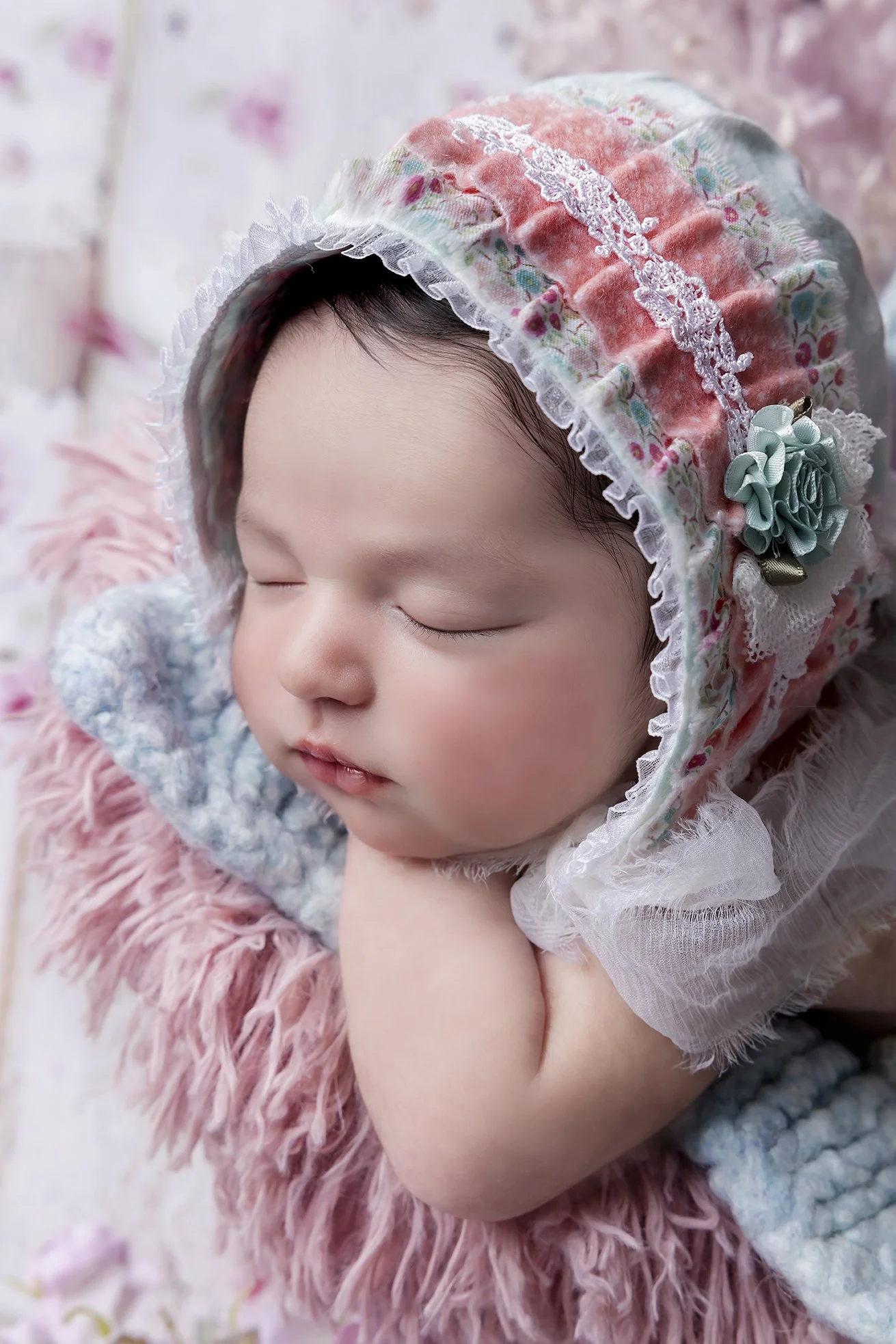 A sleeping baby with a floral bonnet resting on a pink fluffy blanket.