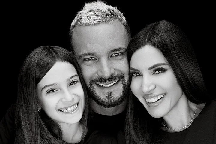 Black and white close-up photo of three smiling people, a man in the middle with light hair and a beard, flanked by two women with dark hair.