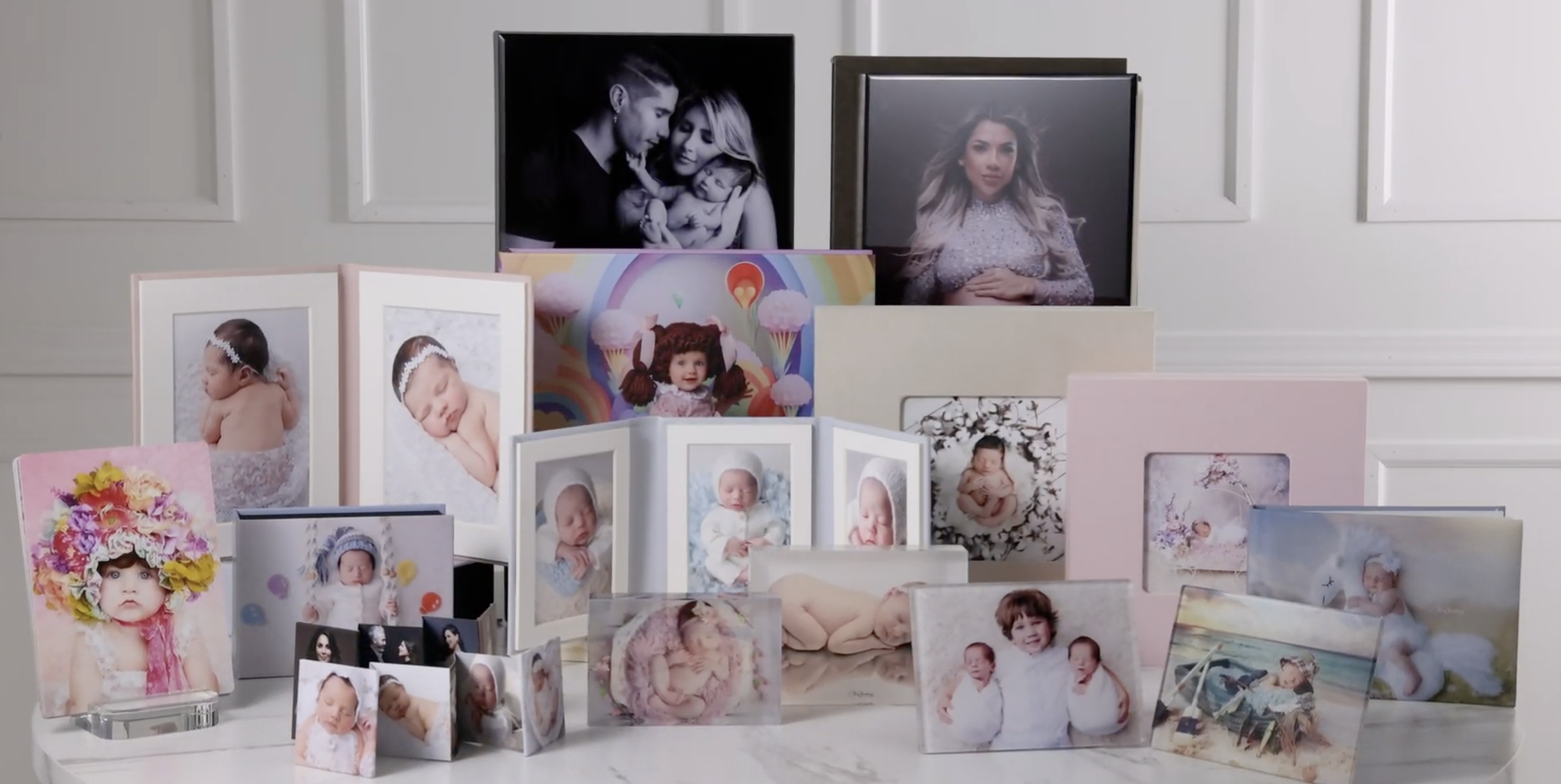 A collection of framed photographs of babies, children, and family portraits arranged on a white surface against a neutral background.