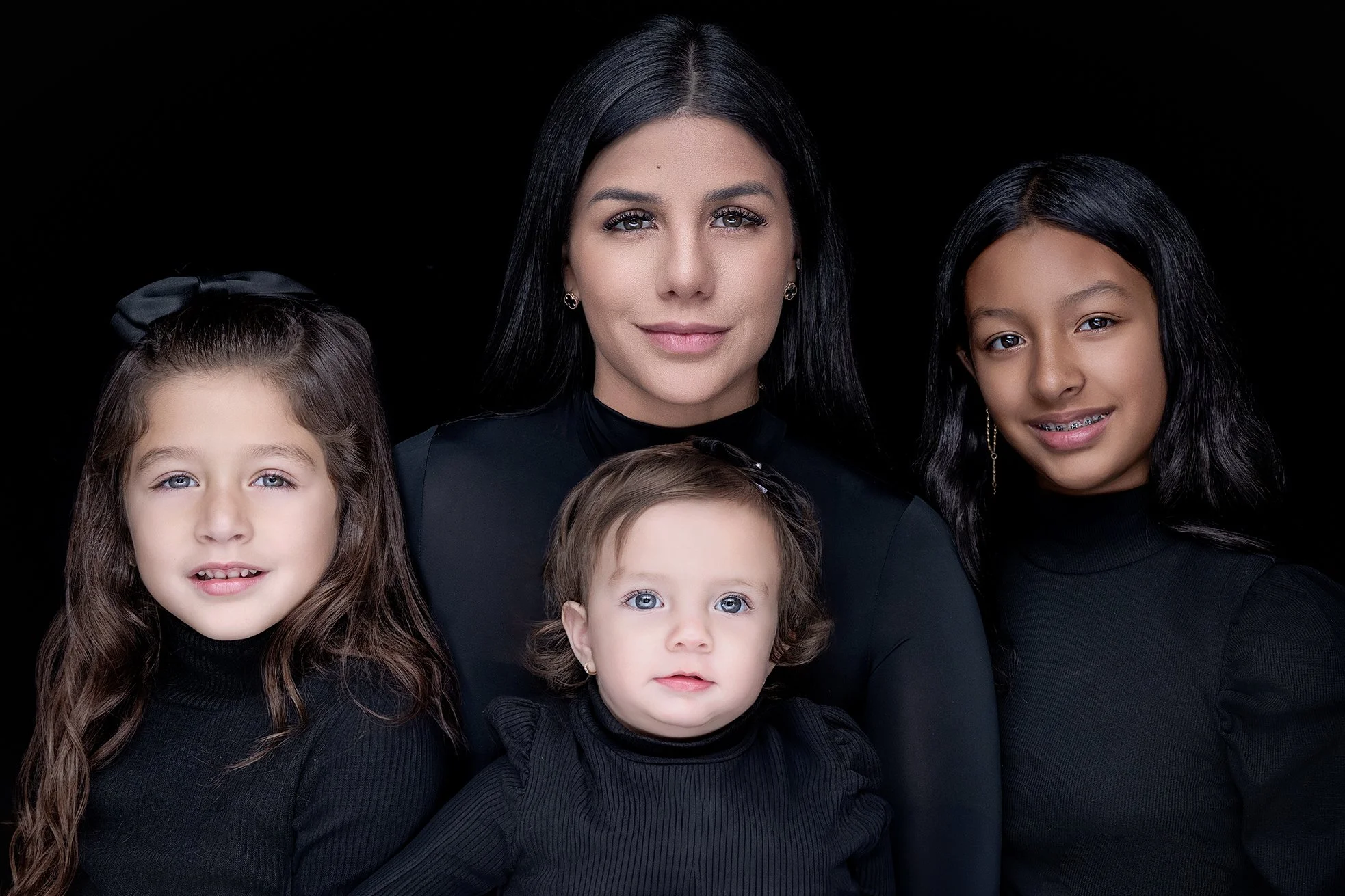 A woman with three young girls all wearing black tops, posing against a black background.