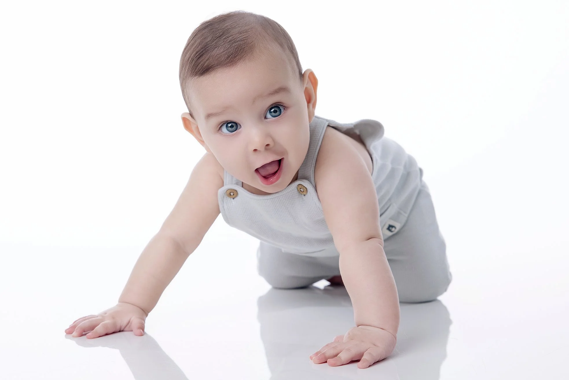 A baby crawling on a white surface, looking at the camera with a surprised expression.
