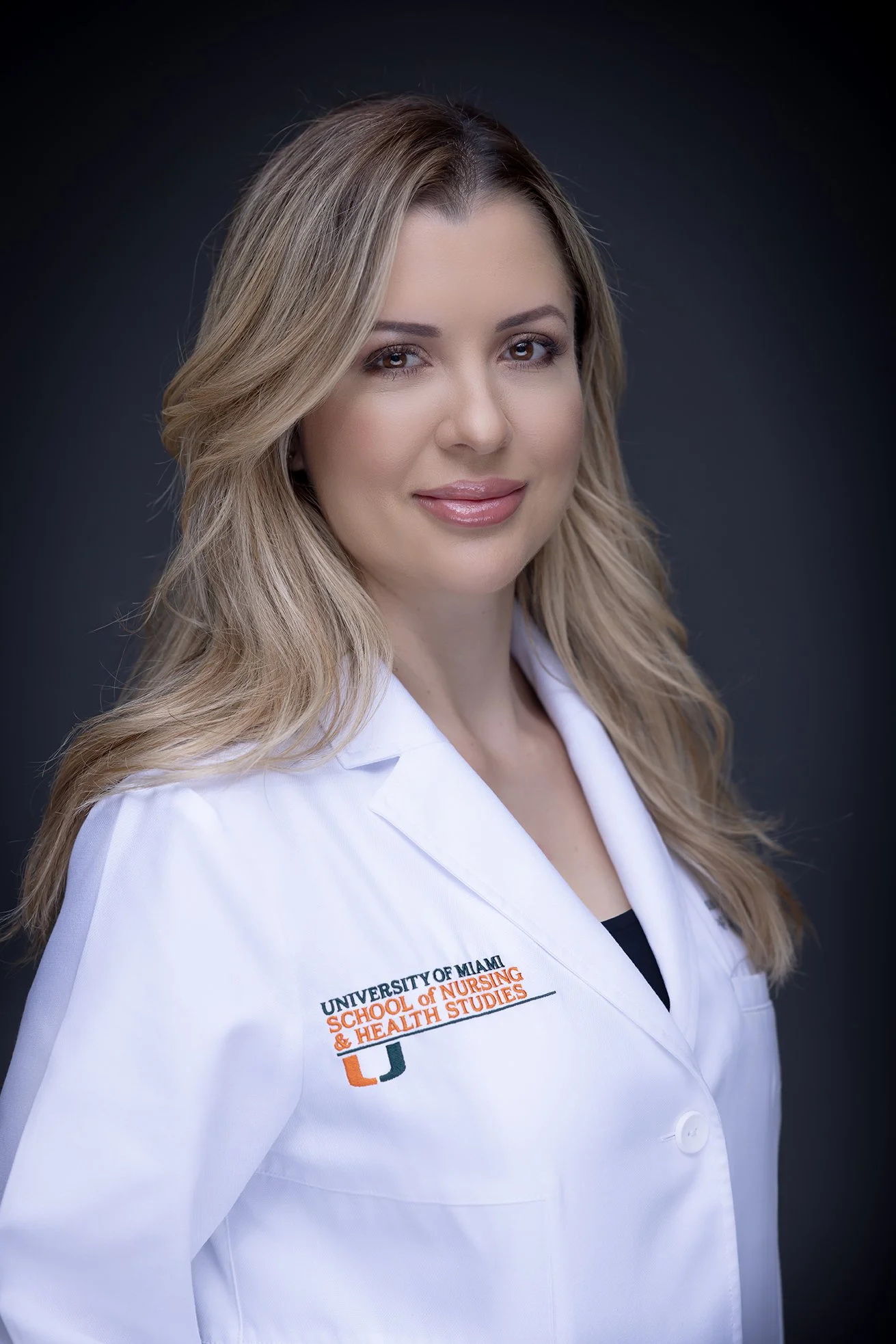 Portrait of a woman in a white medical coat with University of Miami School of Nursing and Health Studies logo, against a dark background.