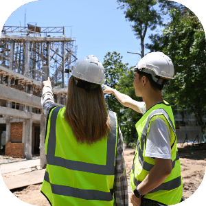 Two construction workers in safety vests and helmets pointing at a building under construction.