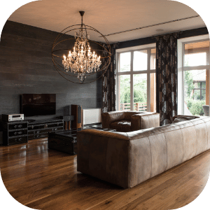 Living room with a large chandelier, a leather sofa, a TV, and large windows with patterned curtains, hardwood floors.