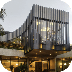 Modern building with curved architectural design featuring vertical slats and large glass windows, with interior lighting visible.