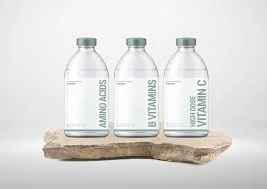 Three clear glass bottles labeled 'Amino Acids,' 'Vitamins,' and 'Vitamin C' on a wooden board against a white background.