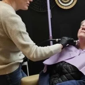 Close-up of a woman receiving a facial injection, with a syringe near her cheek and her eyes closed.