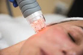 A woman receiving a facial treatment with a skincare device applied to her face in a spa or clinic setting.