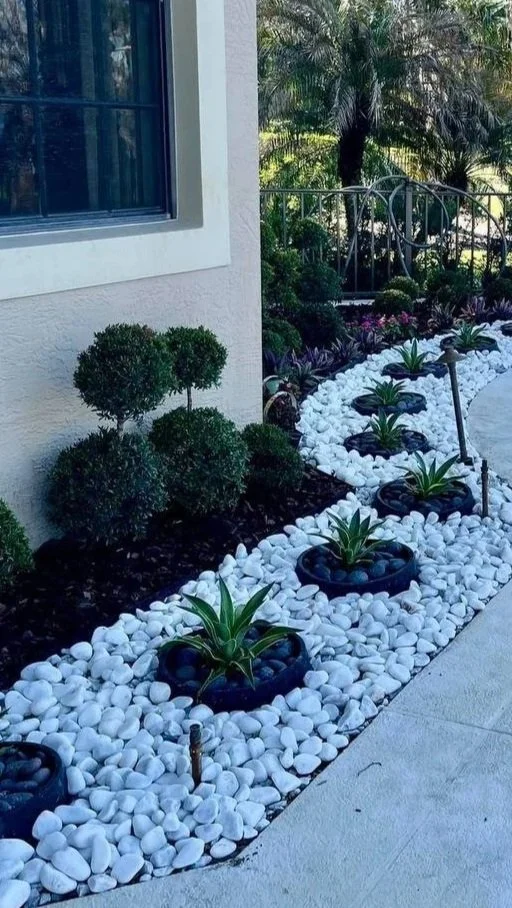 White marble pebbles installed in a narrow succulent bed with black accent bowls