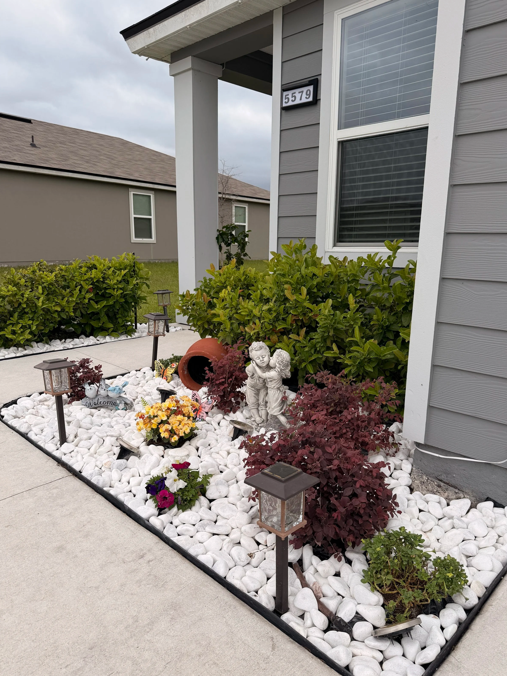 White marble pebbles installed with burgundy foliage, flowers, solar lights, and garden ornaments