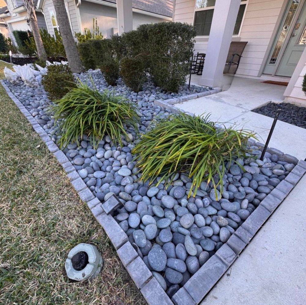 Black Mexican beach pebbles installed in a gray-bordered residential landscape bed