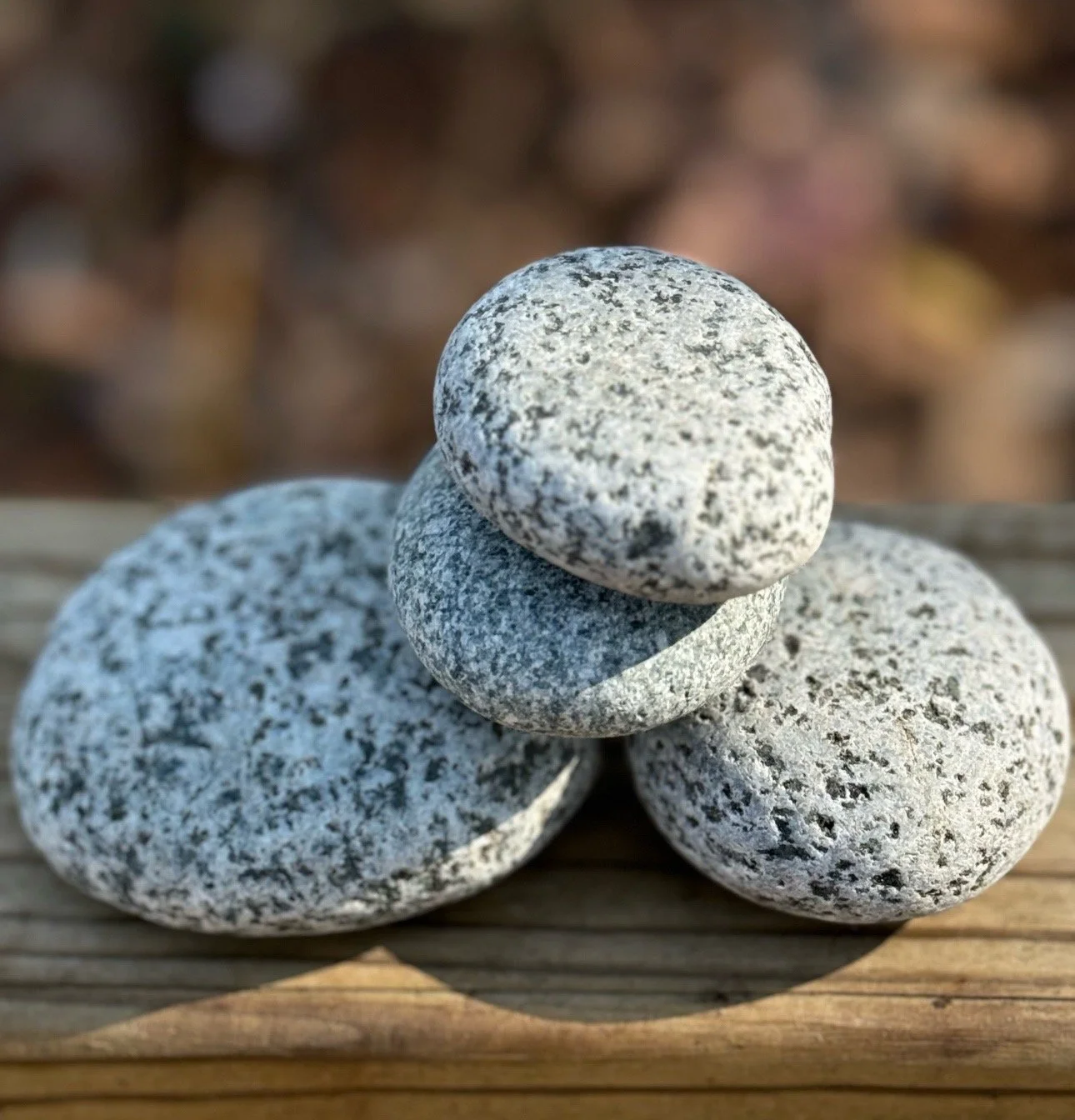Three gray speckled stones stacked on a wooden surface with a blurred natural background.