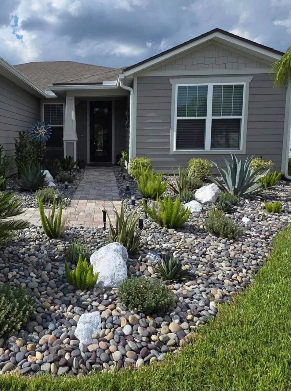 Mixed Mexican beach pebbles installed in a front-yard succulent bed with boulders and pavers