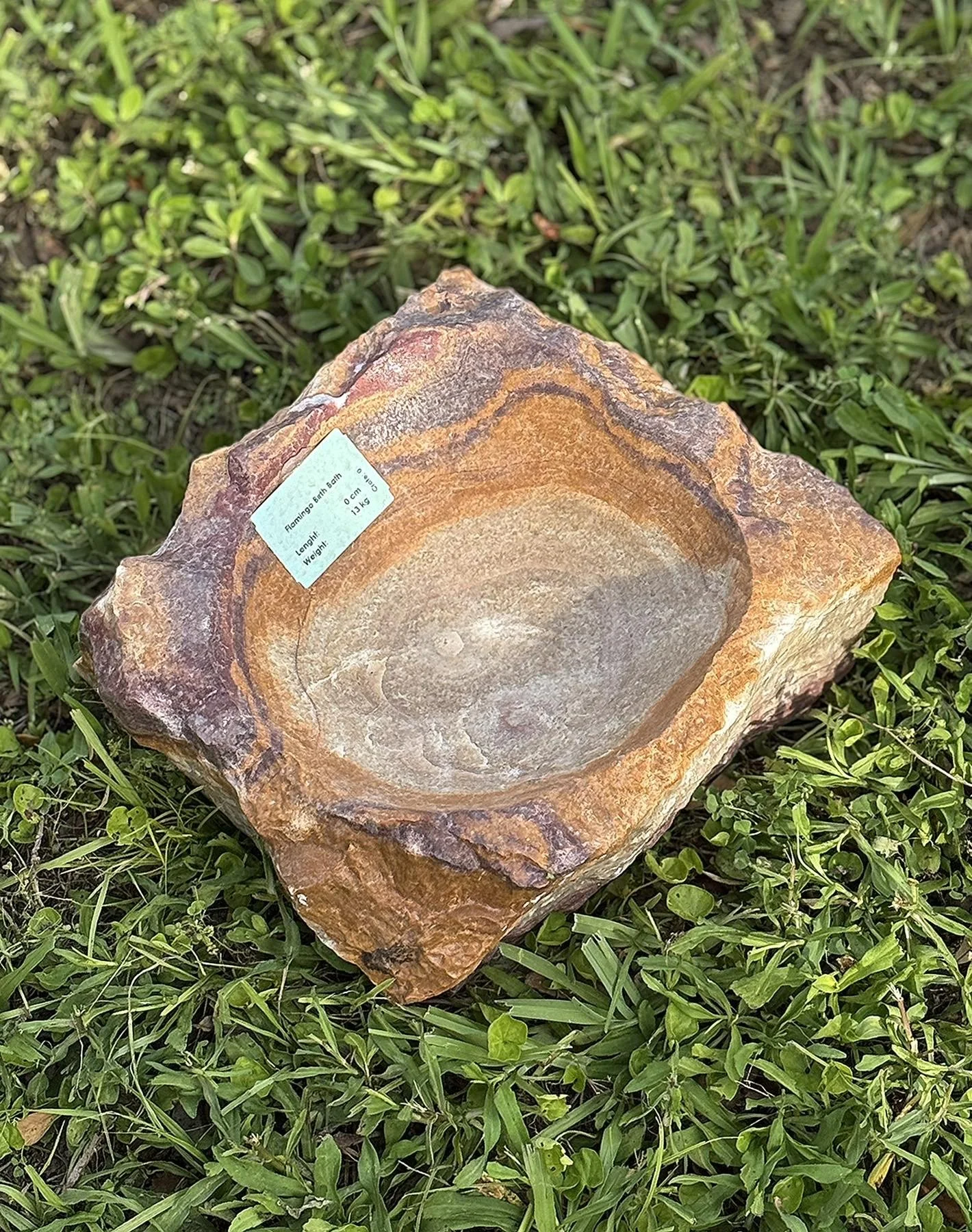 A large piece of sandstone rock with a shallow carved bowl in the center, placed on green grass.
