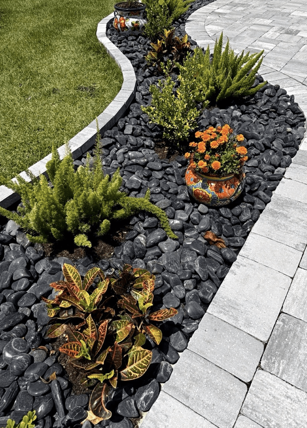Black high-polished pebbles installed beside light pavers with tropical plants and a decorative planter