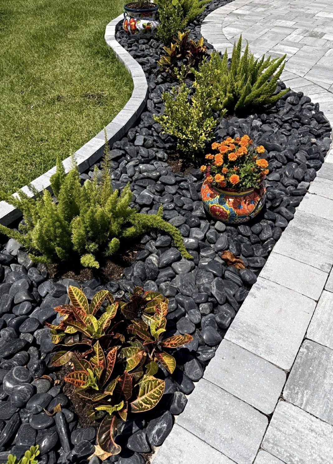 Black high-polished pebbles installed beside light pavers with tropical plants and a decorative planter