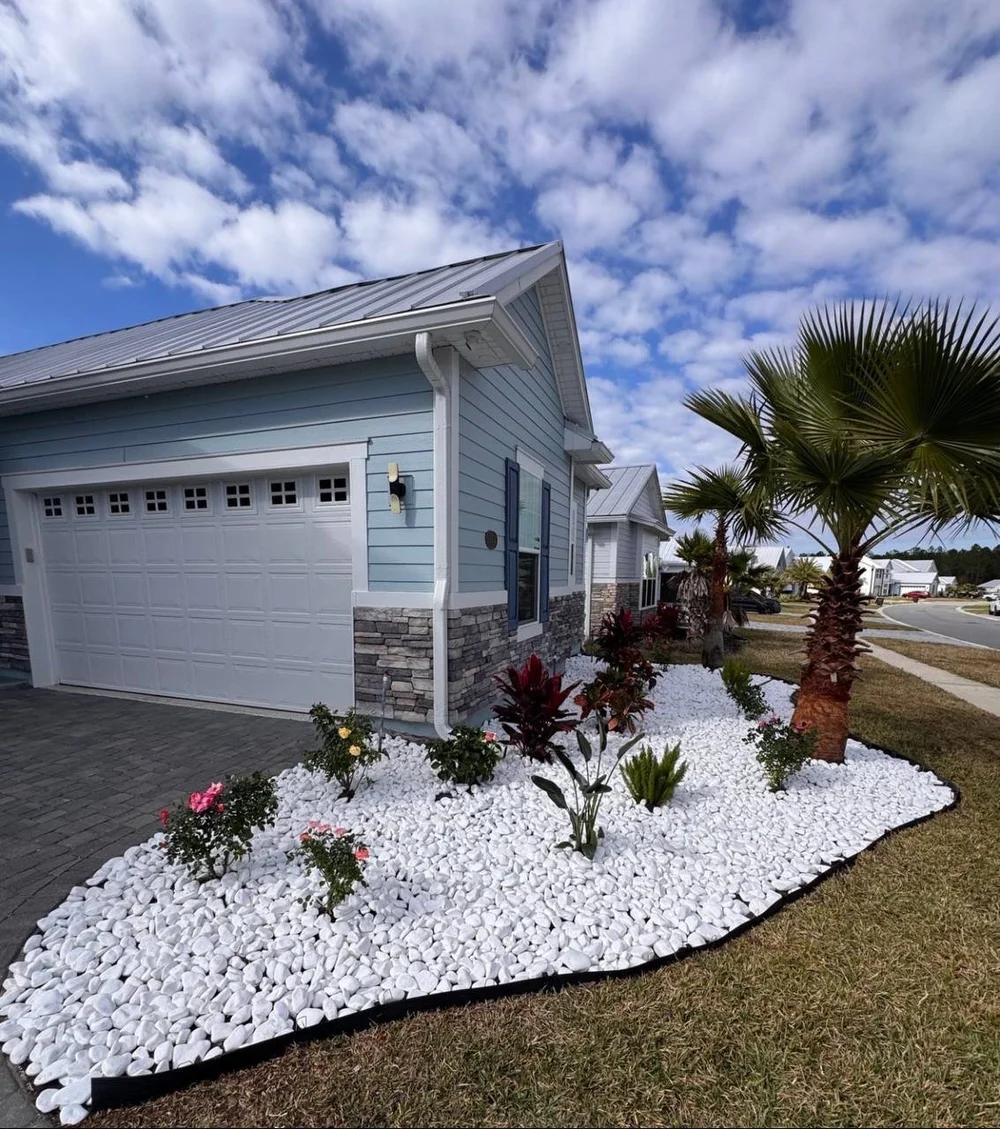 White marble pebbles surrounding palms and flowering plants at a coastal-style home