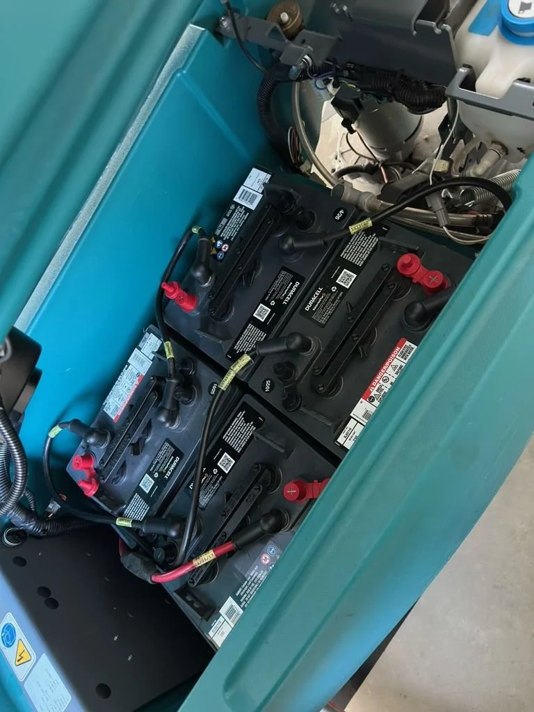 Multiple automotive batteries connected with cables inside a teal-colored equipment container.