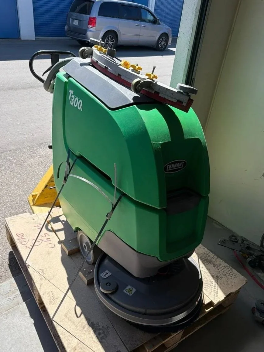Green Tennant T300e floor cleaning machine on a wooden pallet outside a building.