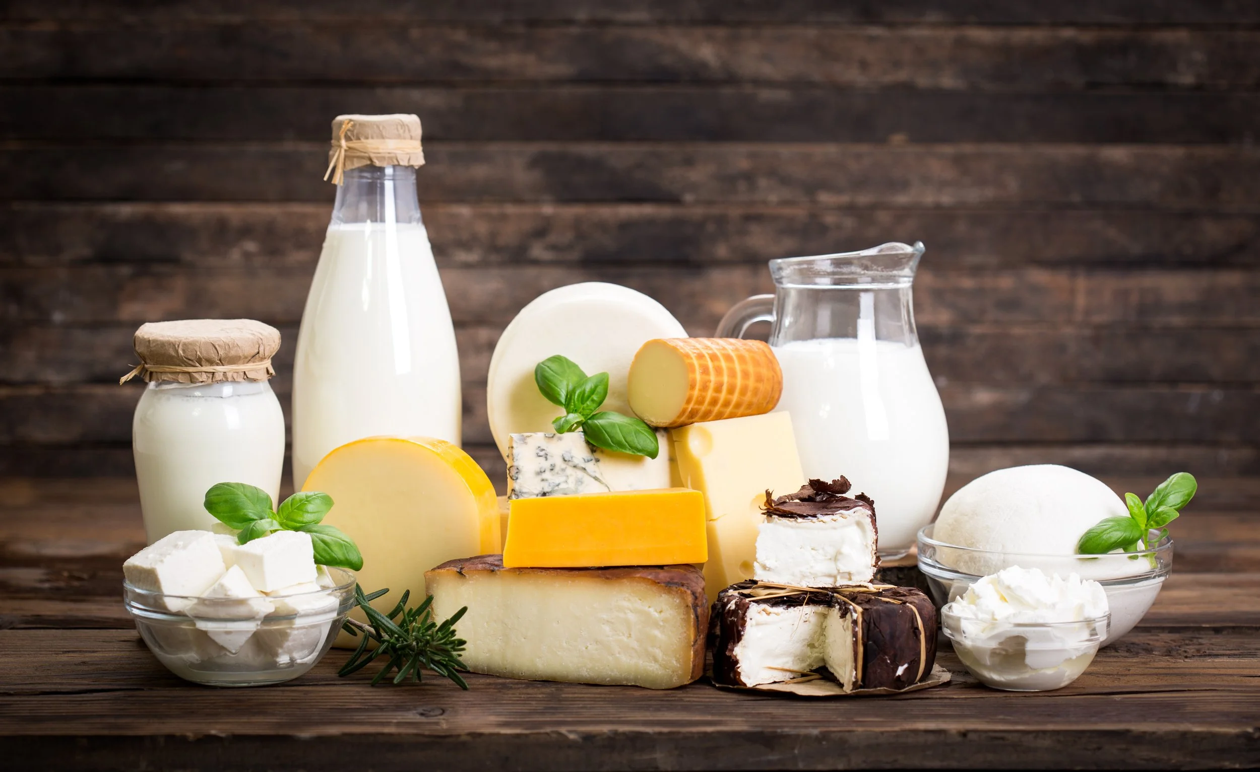 Assorted cheeses, milk, and dairy products on a wooden surface with a rustic background.