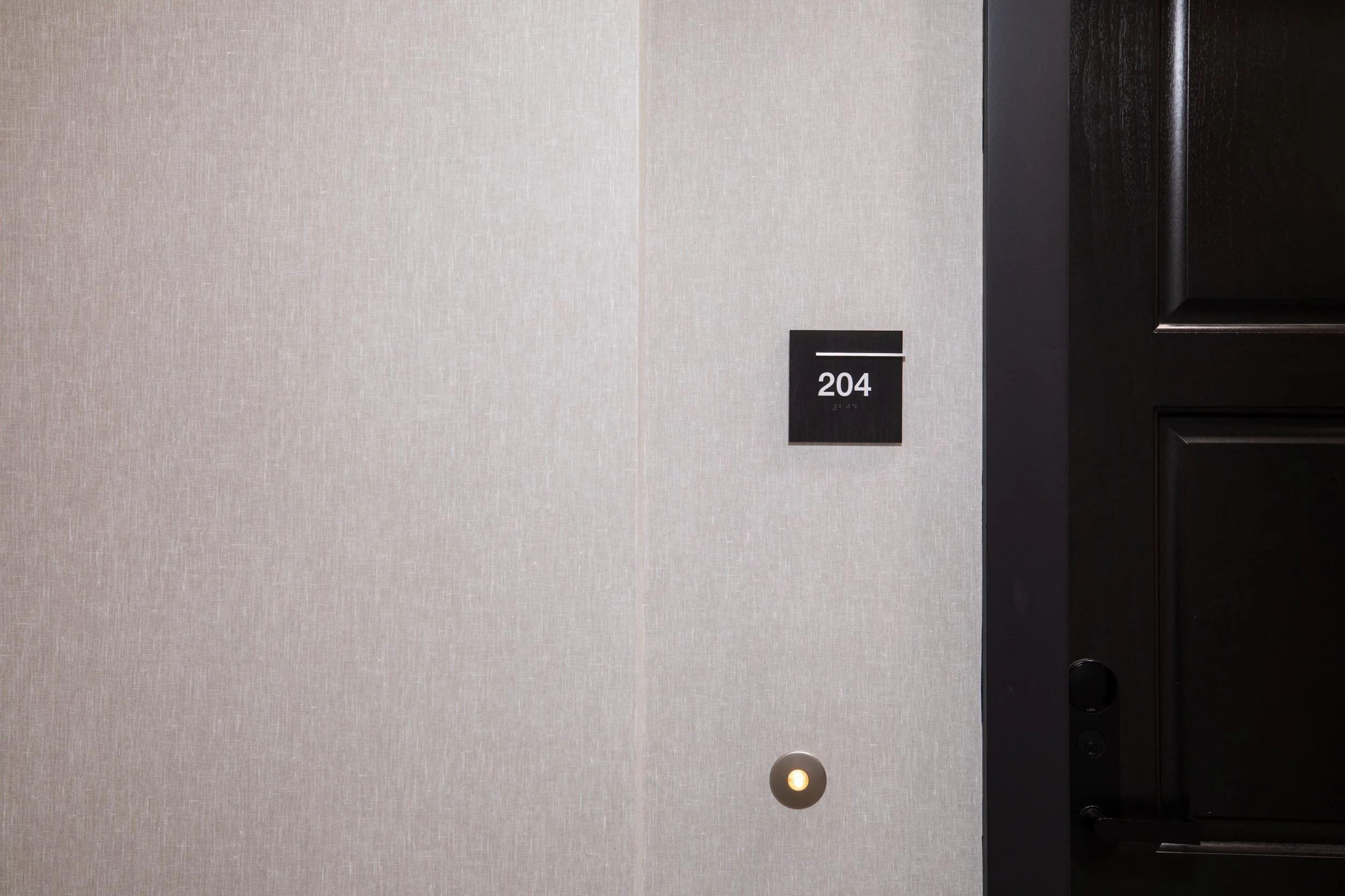 Close-up of awall with a black floor number panel reading 204, a circular door bell with indicator light, and a black door frame.
