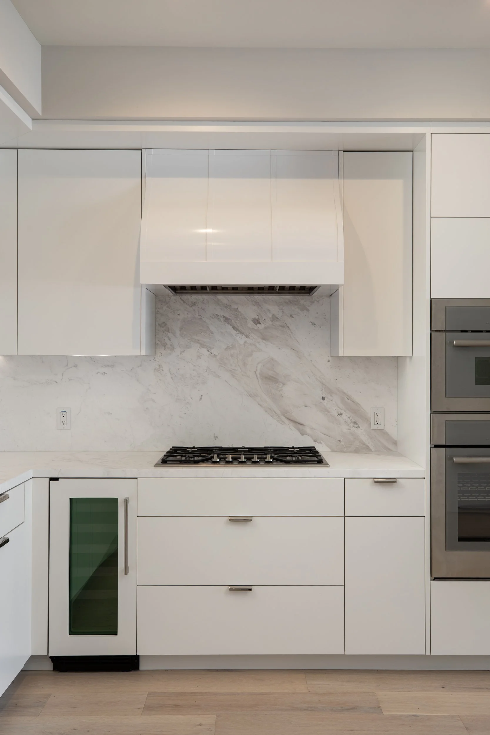 Modern white kitchen with marble backsplash and built-in appliances.