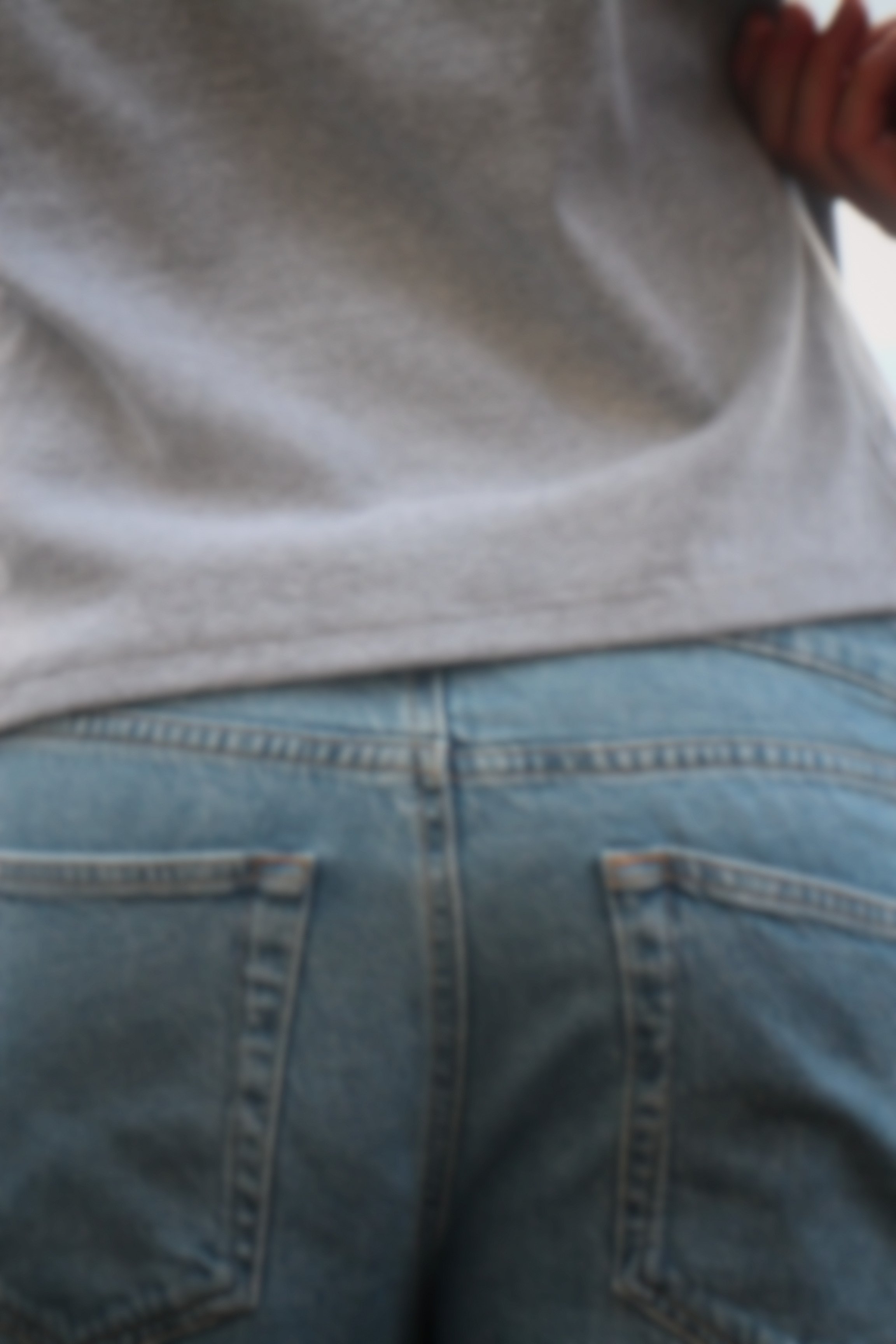 Partie basse d'une personne portant un jean et un haut gris, avec un fond de sol en carrelage.