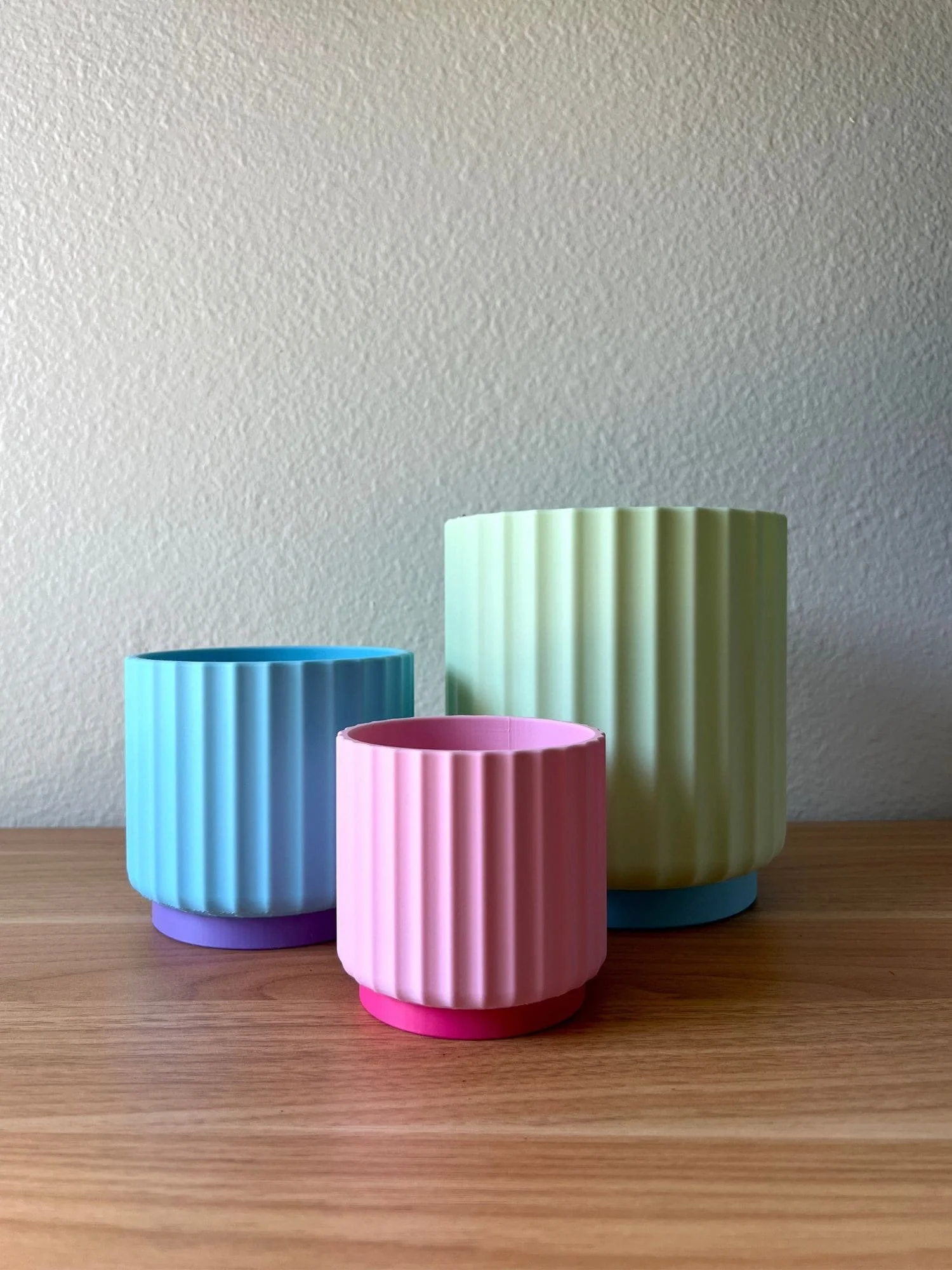 colorful planters, light pink, blue, and green, on a wood desk