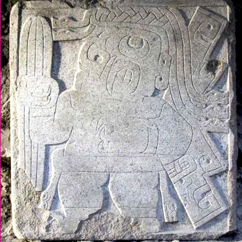 Carved stone tablet depicting a figure riding an animal, with intricate geometric patterns and symbols around the figure.