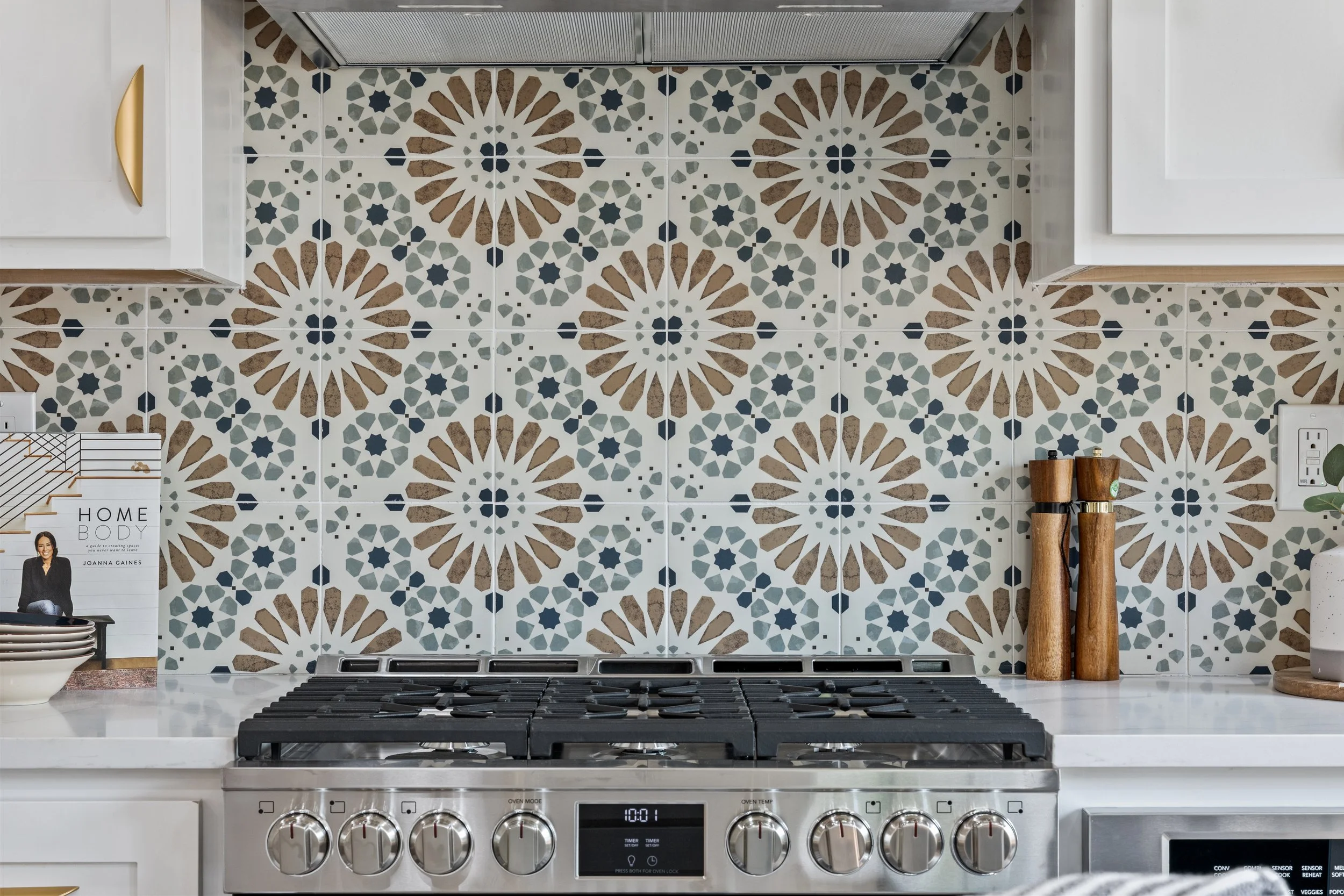 Kitchen backsplash with patterned tiles in brown, blue, and white, above a stainless steel gas stove with six burners and control knobs.