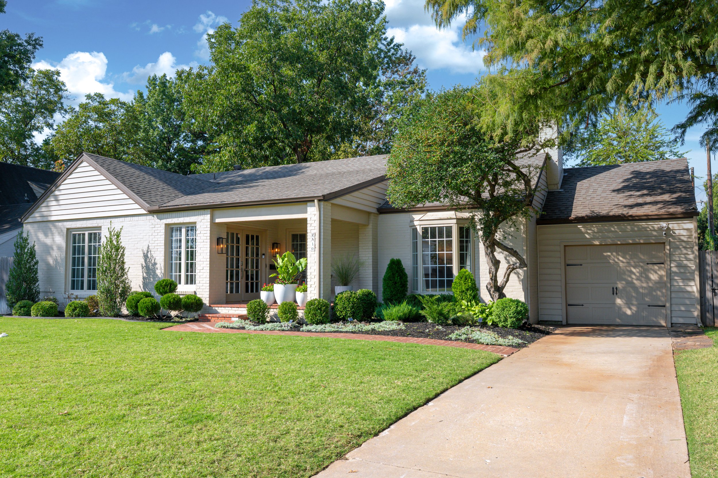 Front view of a suburban house with a manicured lawn, a paved driveway, and lush green trees.
