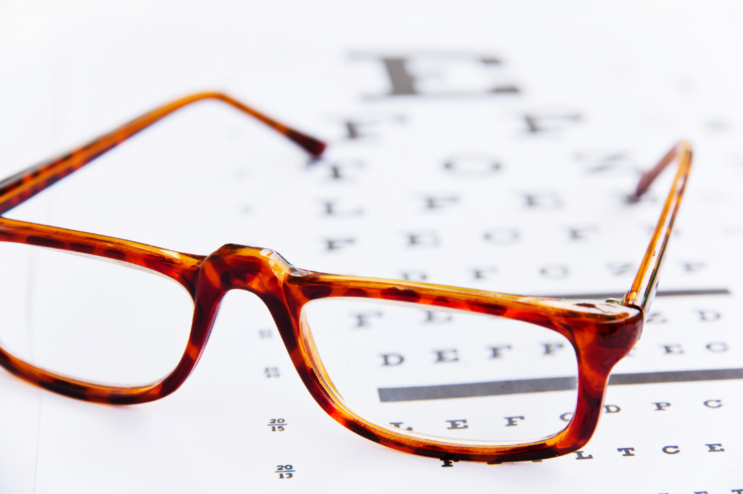 A pair of tortoiseshell eyeglasses resting on an eye chart.
