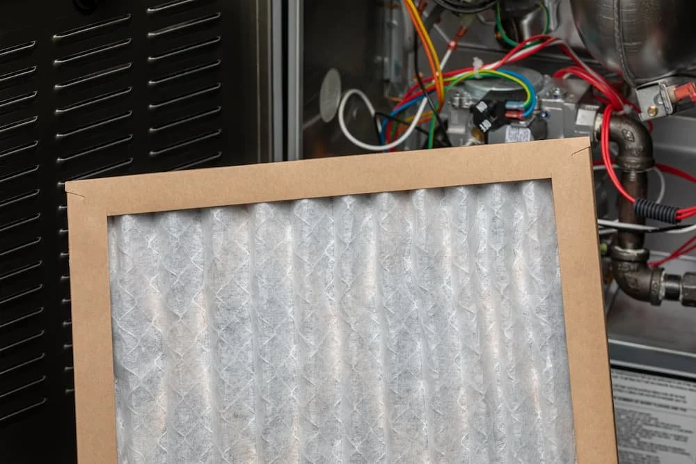 A close-up of a new pleated furnace air filter being installed into an HVAC system, highlighting the importance of regular furnace filter replacement for home air quality.