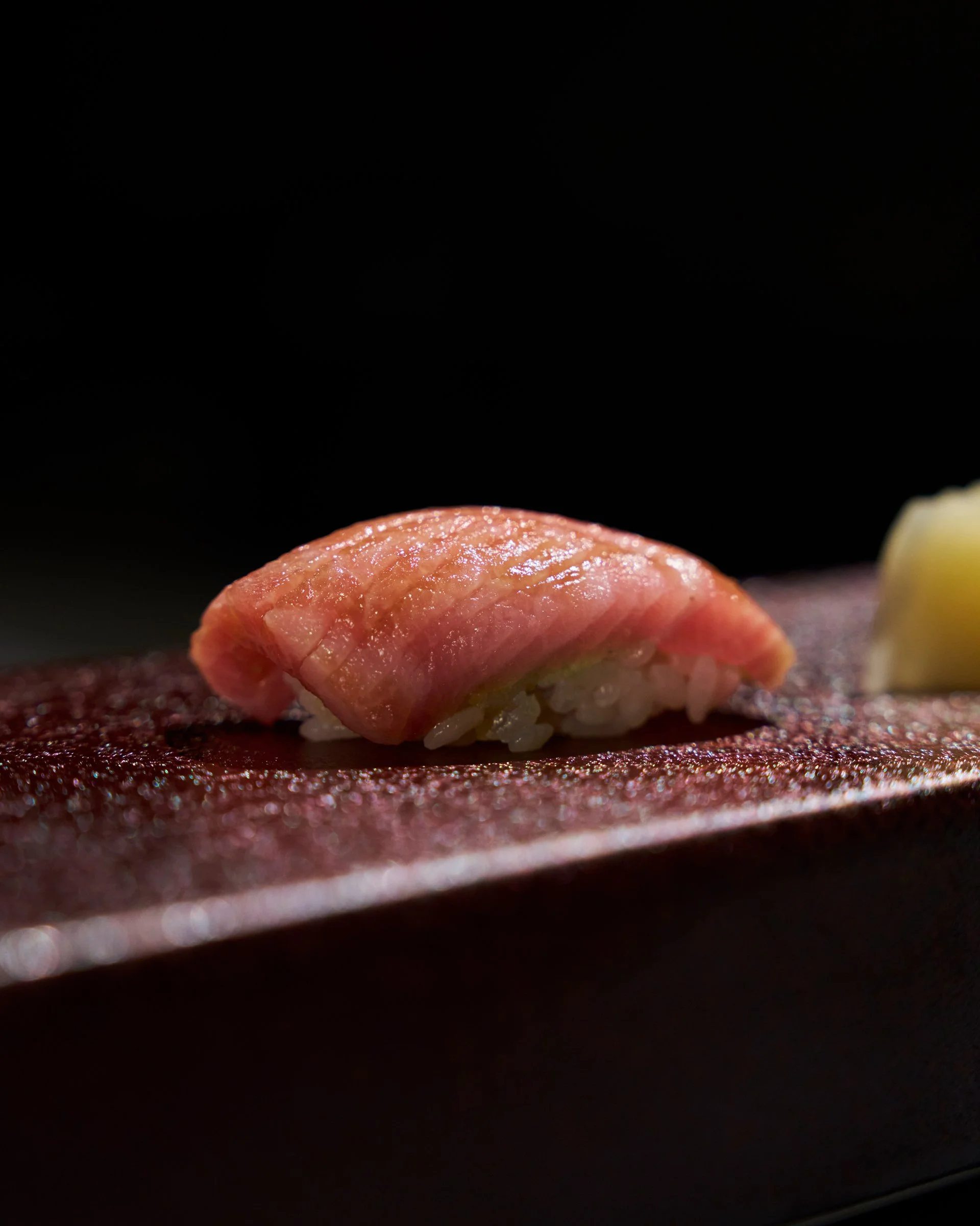 A close-up of a piece of sushi with fish on top, placed on a textured surface with a lemon wedge in the background.