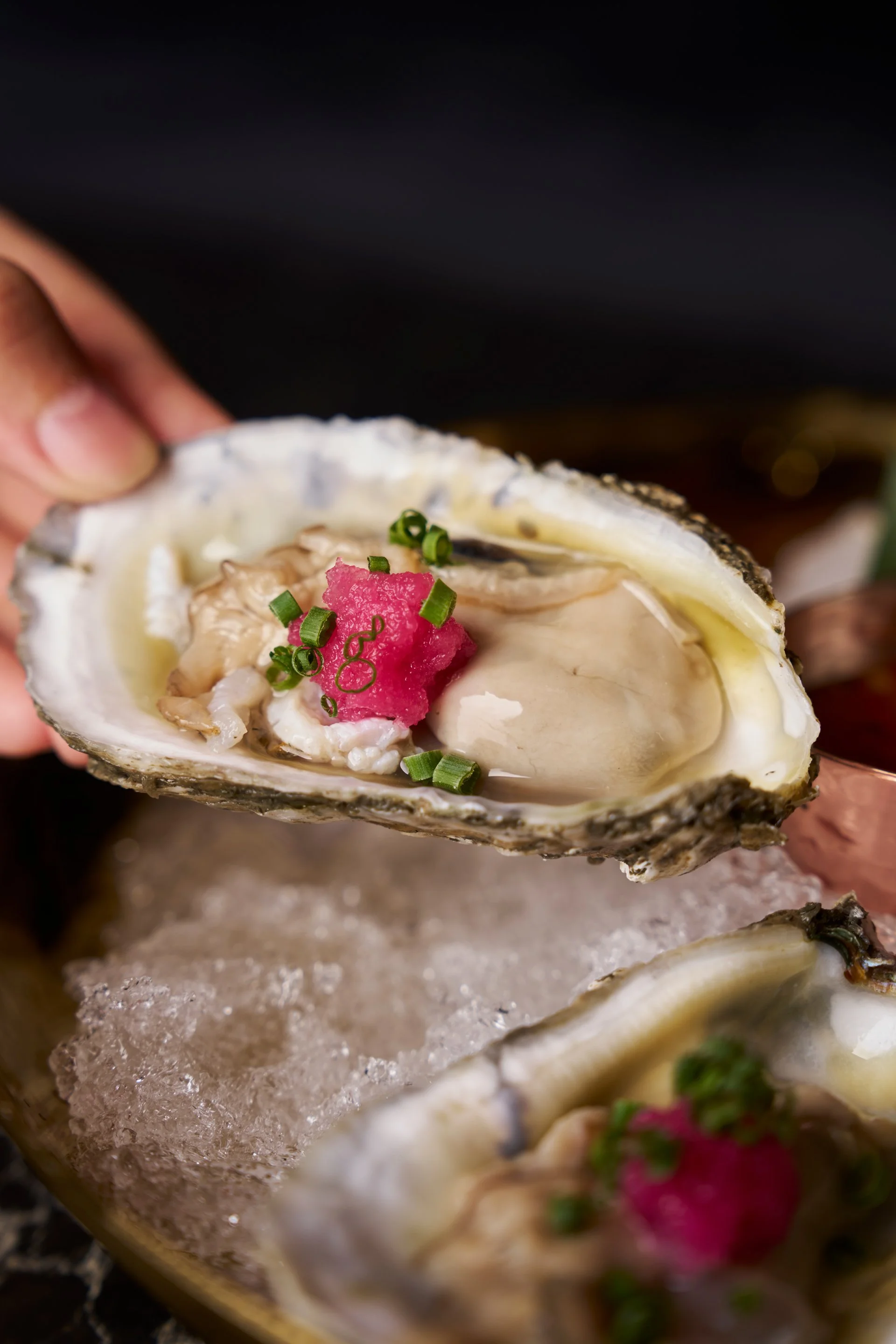 A fresh oyster on crushed ice with a garnish of pink radish and chopped green onion.