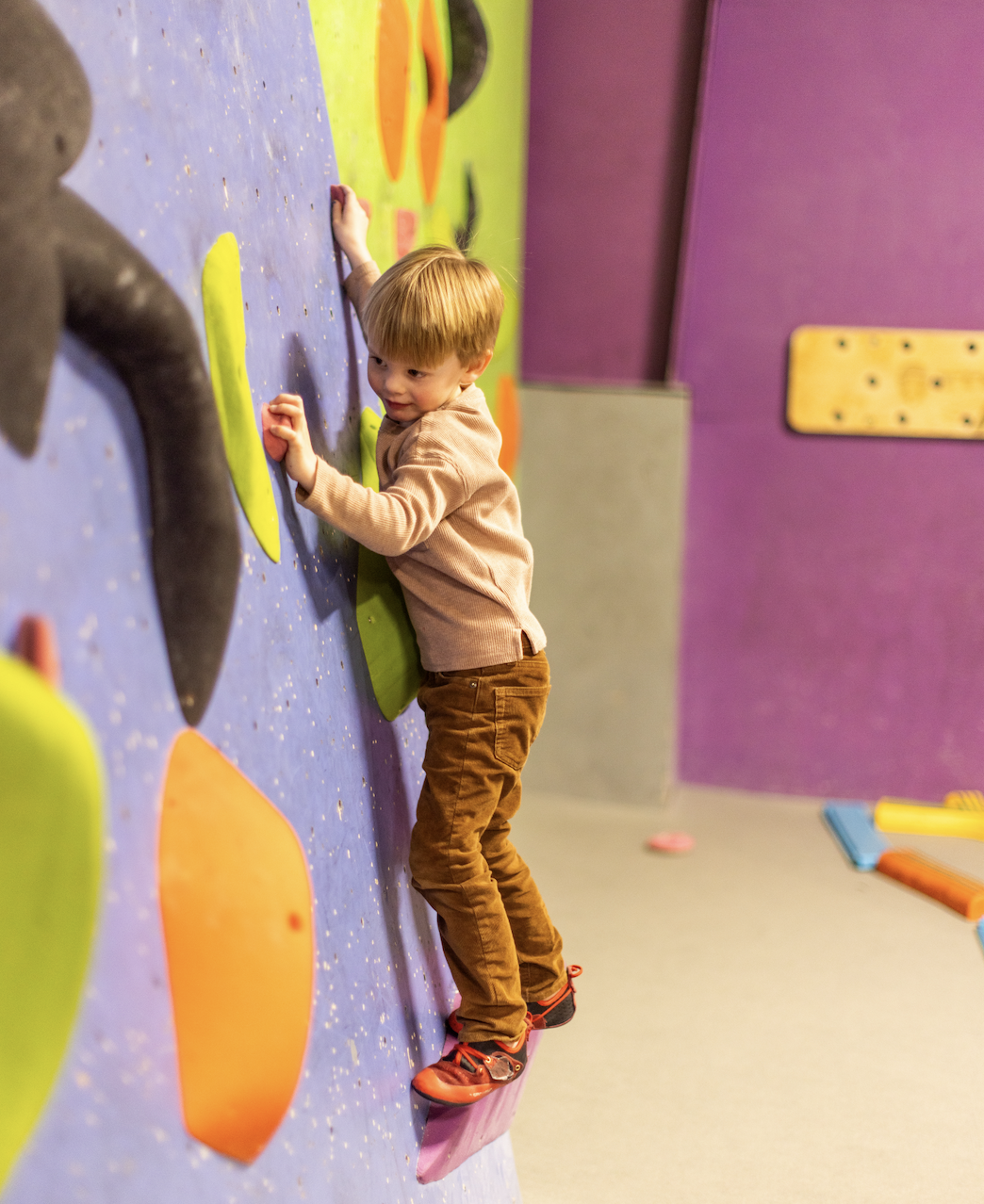 Toddler climbing a colorful wall on his first visit to ABC Kids Climbing in Boulder