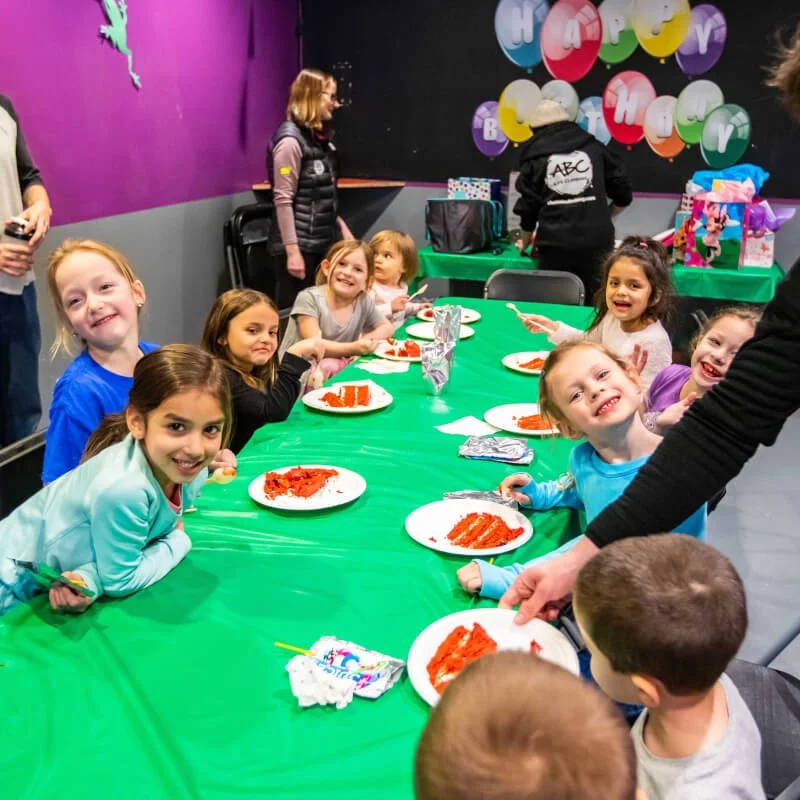 Smiling kids eating pizza at a long table during a climbing birthday party at ABC Kids Climbing in Boulder