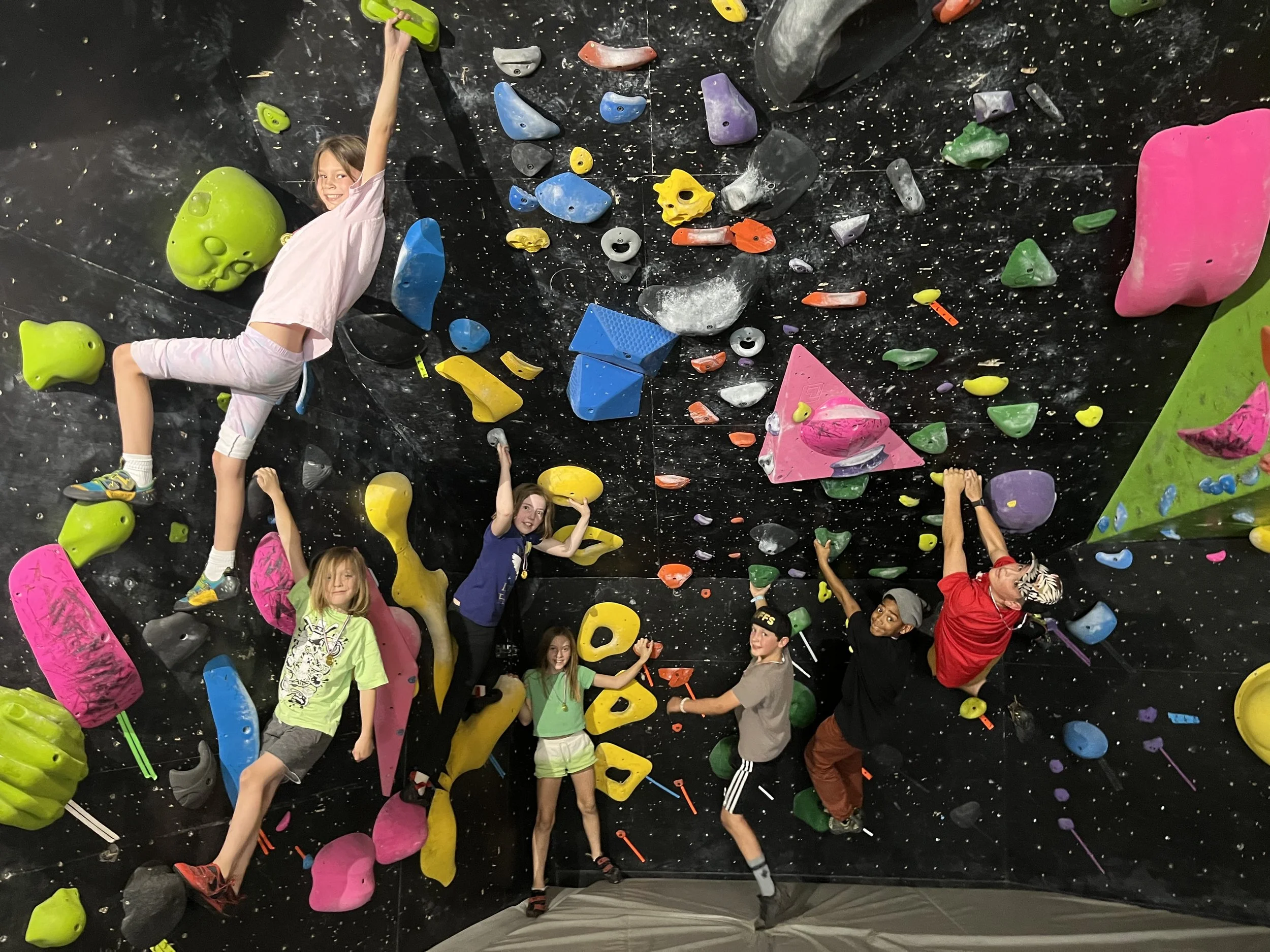 Group of ABC Kids club climbers on a dark wall covered in colorful holds at ABC Kids Climbing in Boulder