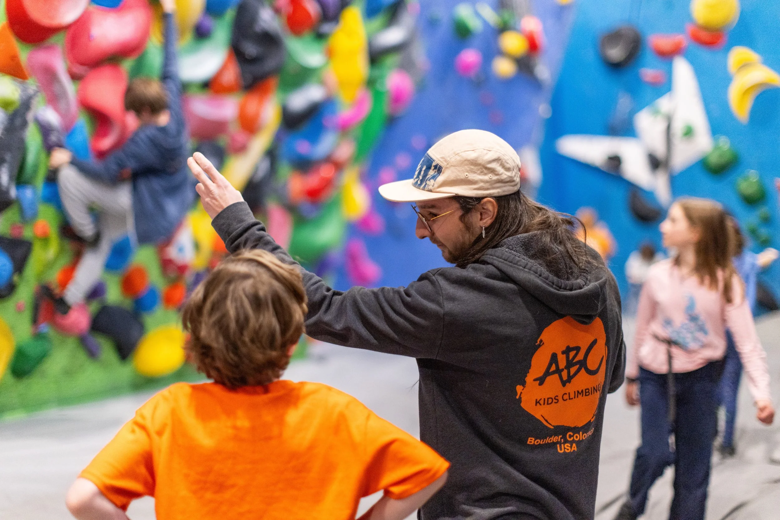 ABC Kids Climbing coach pointing out a route on the bouldering wall to a young climber in an orange shirt