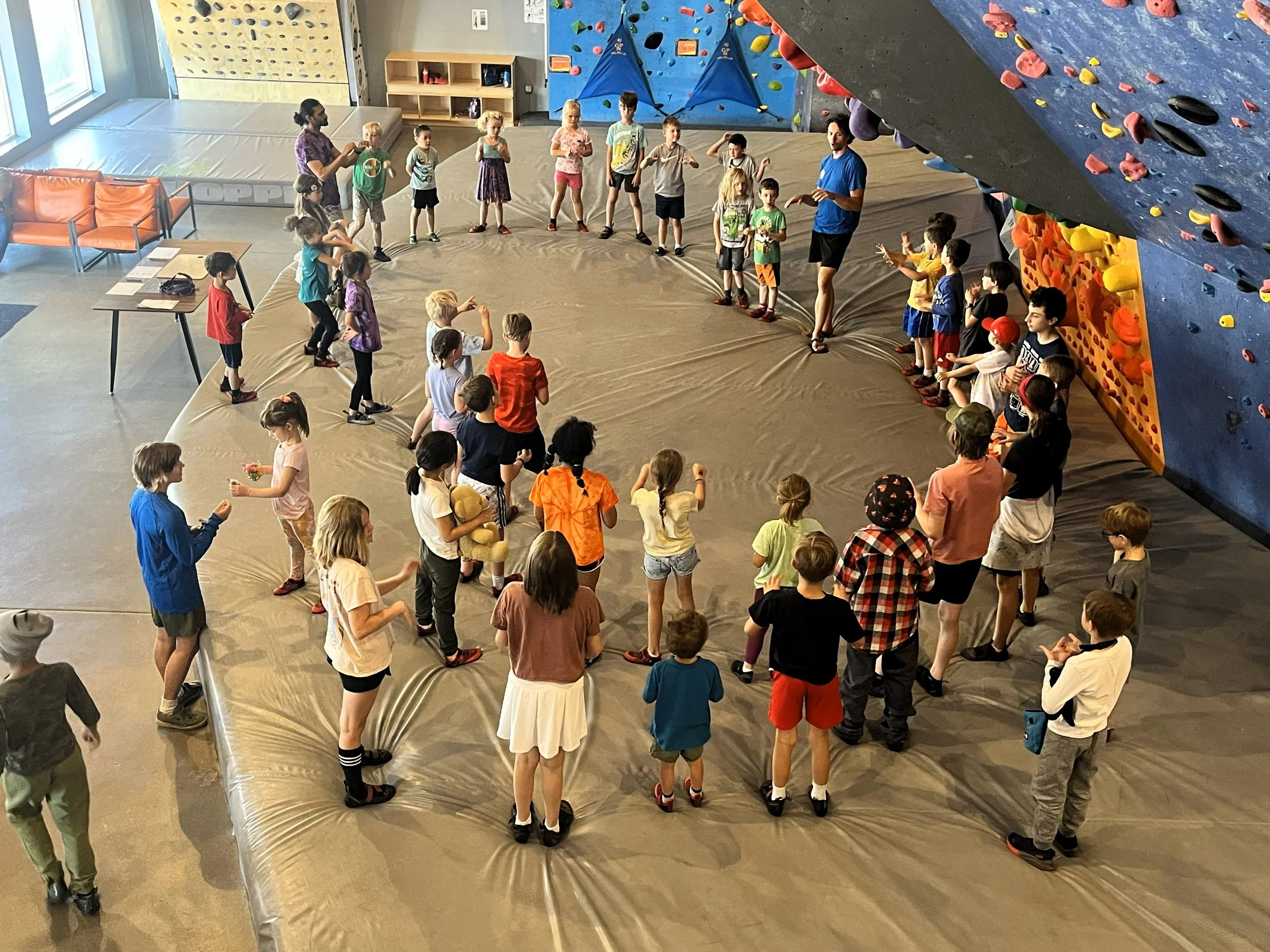 School group of kids gathered in a circle on the gym floor during a field trip to ABC Kids Climbing in Boulder