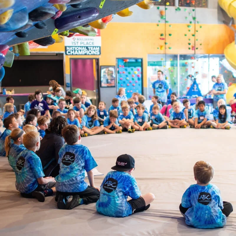 Campers in matching blue tie-dye shirts sitting in a circle at ABC Kids Climbing summer camp in Boulder