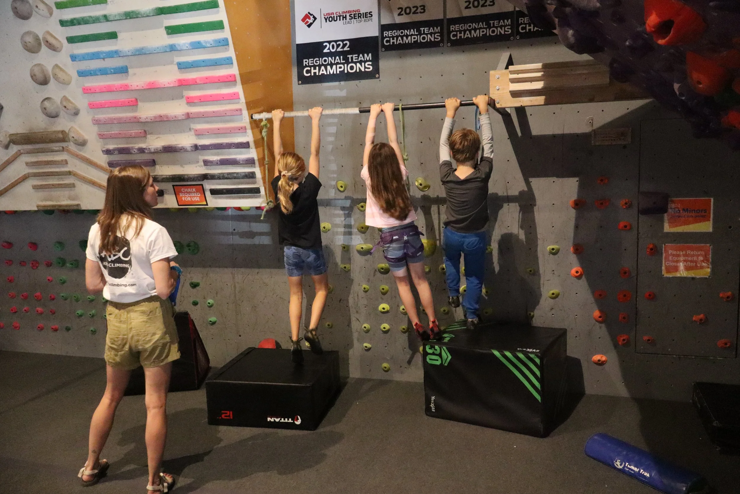 Super Stars team climbers doing hang training on a bar under championship banners at ABC Kids Climbing