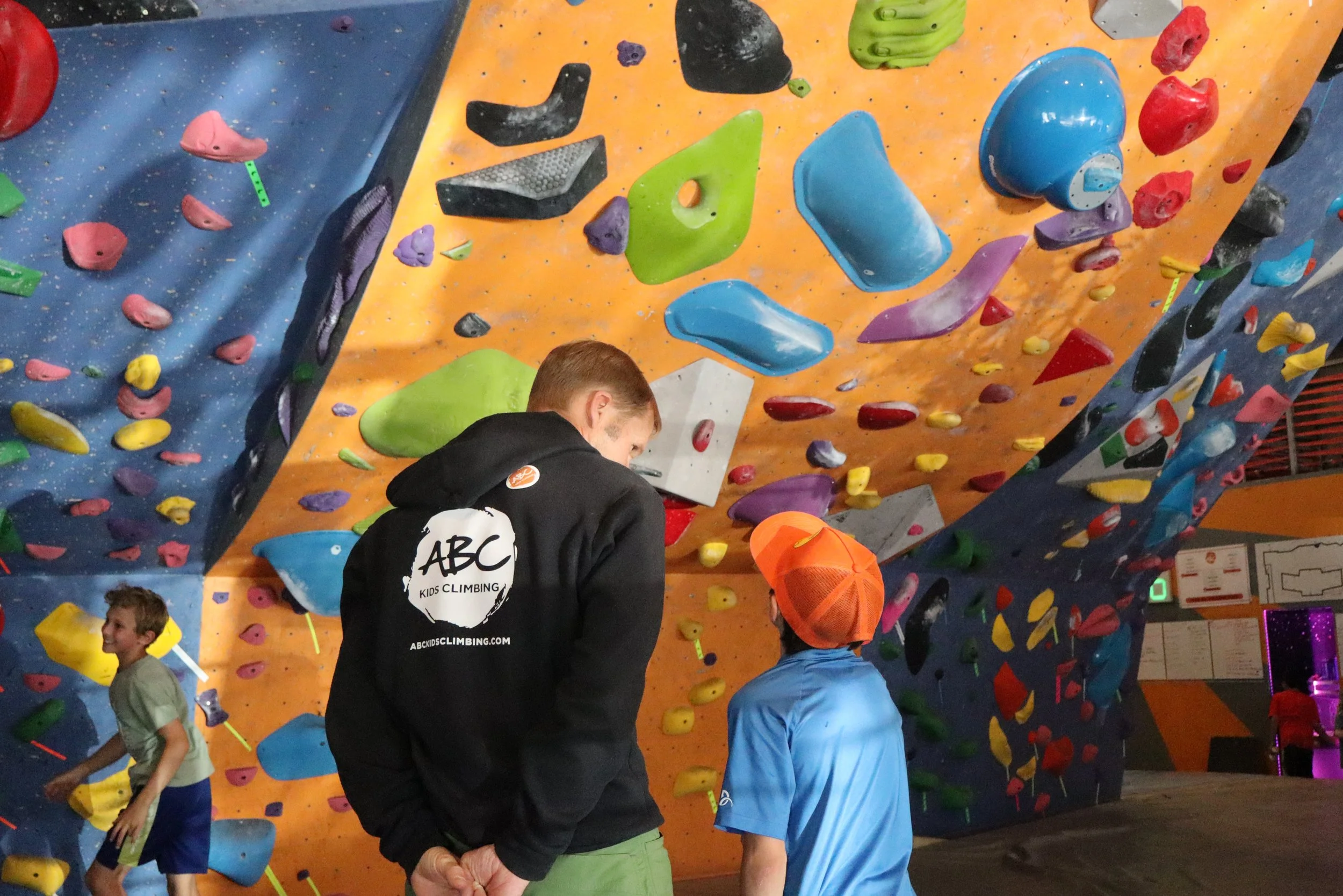 Team ABC Select coach and a young climber in an orange helmet studying a bouldering problem together