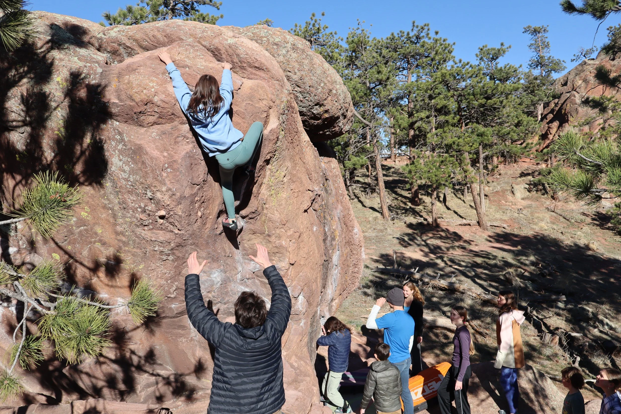 Youth climber bouldering on red sandstone while friends spot below on an ABC Outdoors trip near Boulder, Colorado