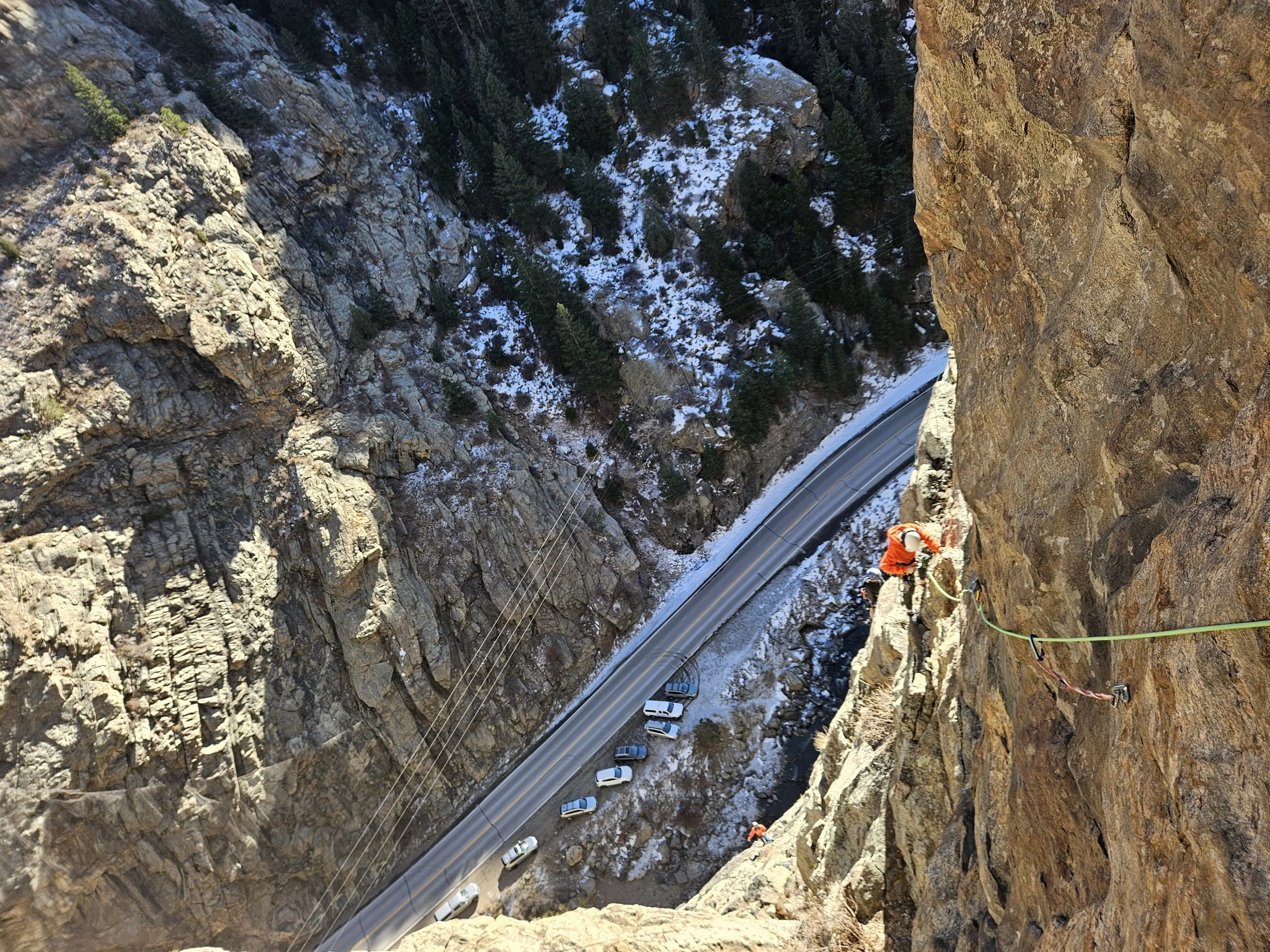 Climber in red high on a canyon wall above a winding road, during ABC outdoor coaching