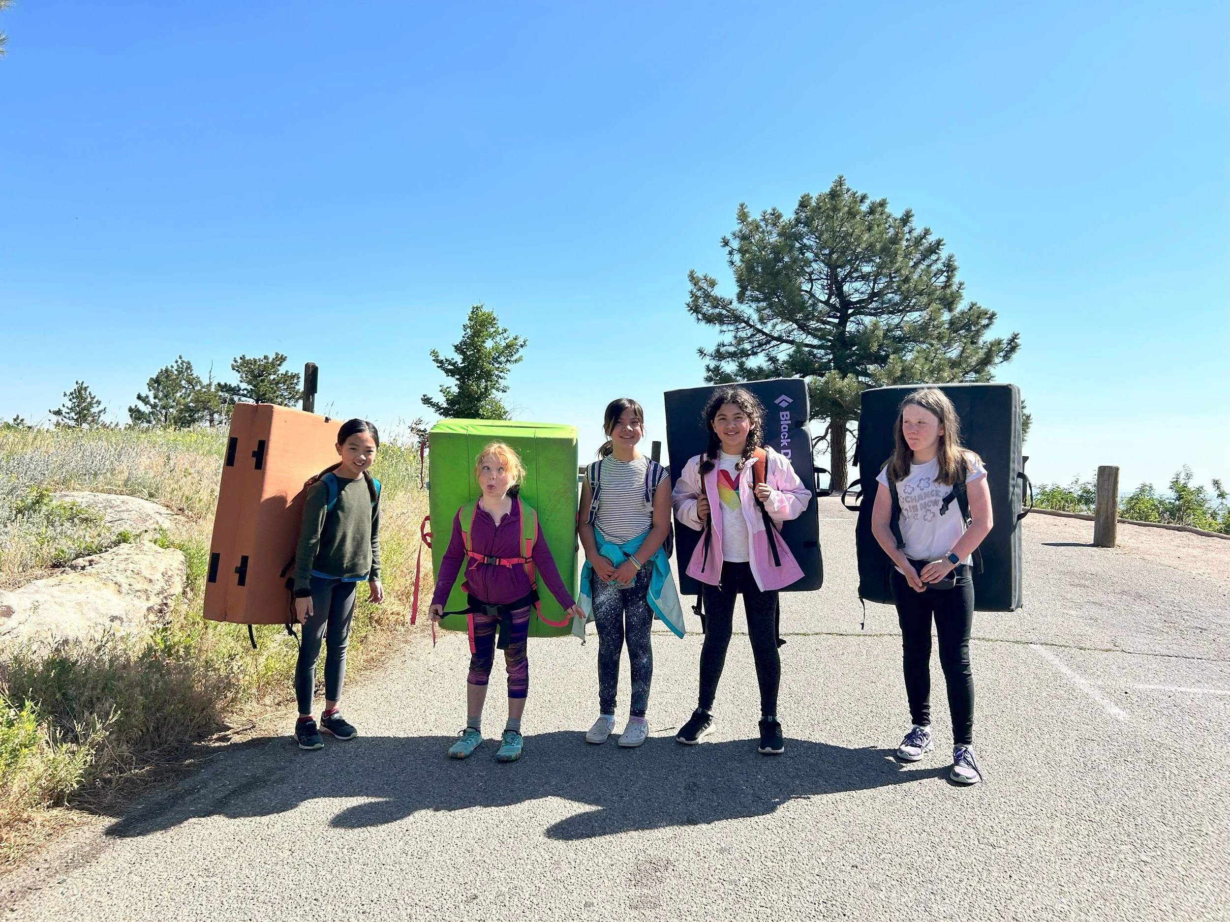 Young campers carrying bouldering crash pads on a trail during ABC indoor/outdoor summer camp near Boulder