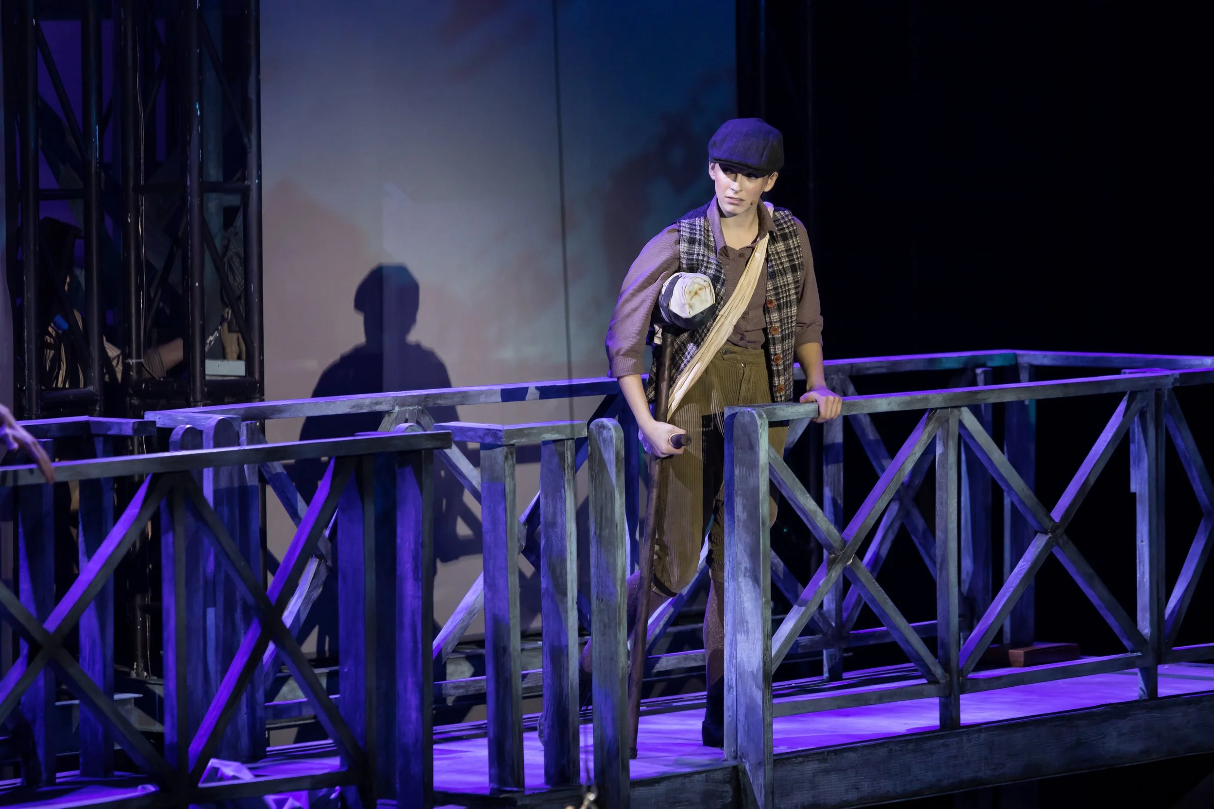 Person dressed in period costume standing on a theater balcony, holding a stick, with a focused expression.