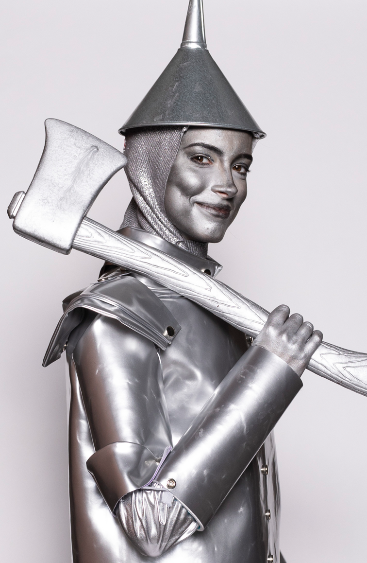 Person dressed as a silver knight, wearing metallic armor, a cone-shaped helmet, and holding an axe over their shoulder, smiling at the camera.