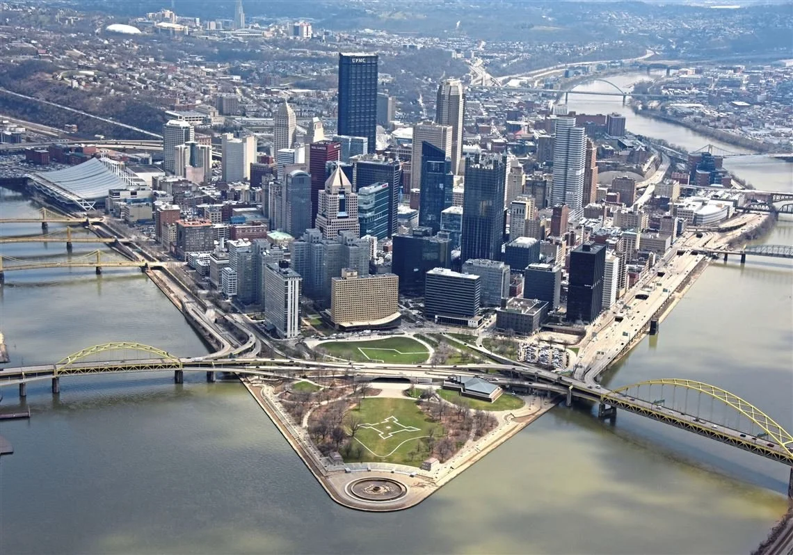 Aerial view of downtown Pittsburgh, Pennsylvania, showing the city skyline, three rivers, bridges, and a park with a circular feature.
